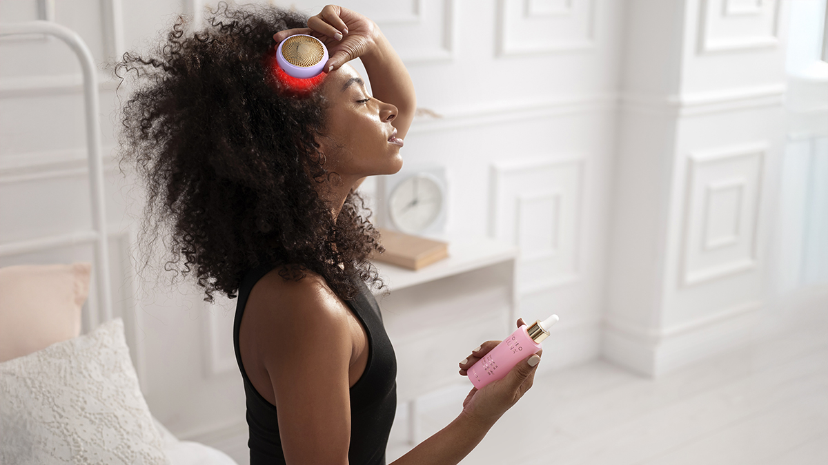 A gorgeous African.American young woman with lush curly hair using red LED light onLUNA 4 hair in a modern white space